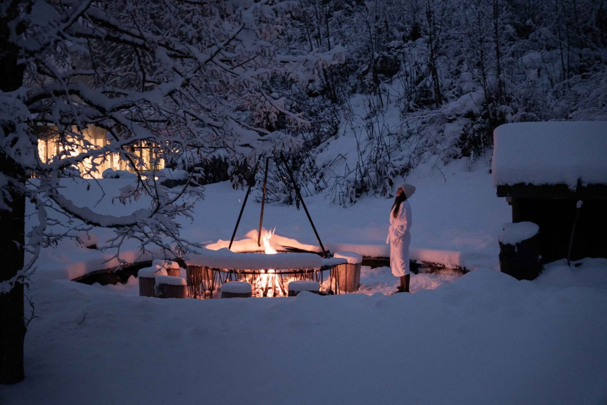 Frau im Bademantel an der Feuerstelle im Schnee