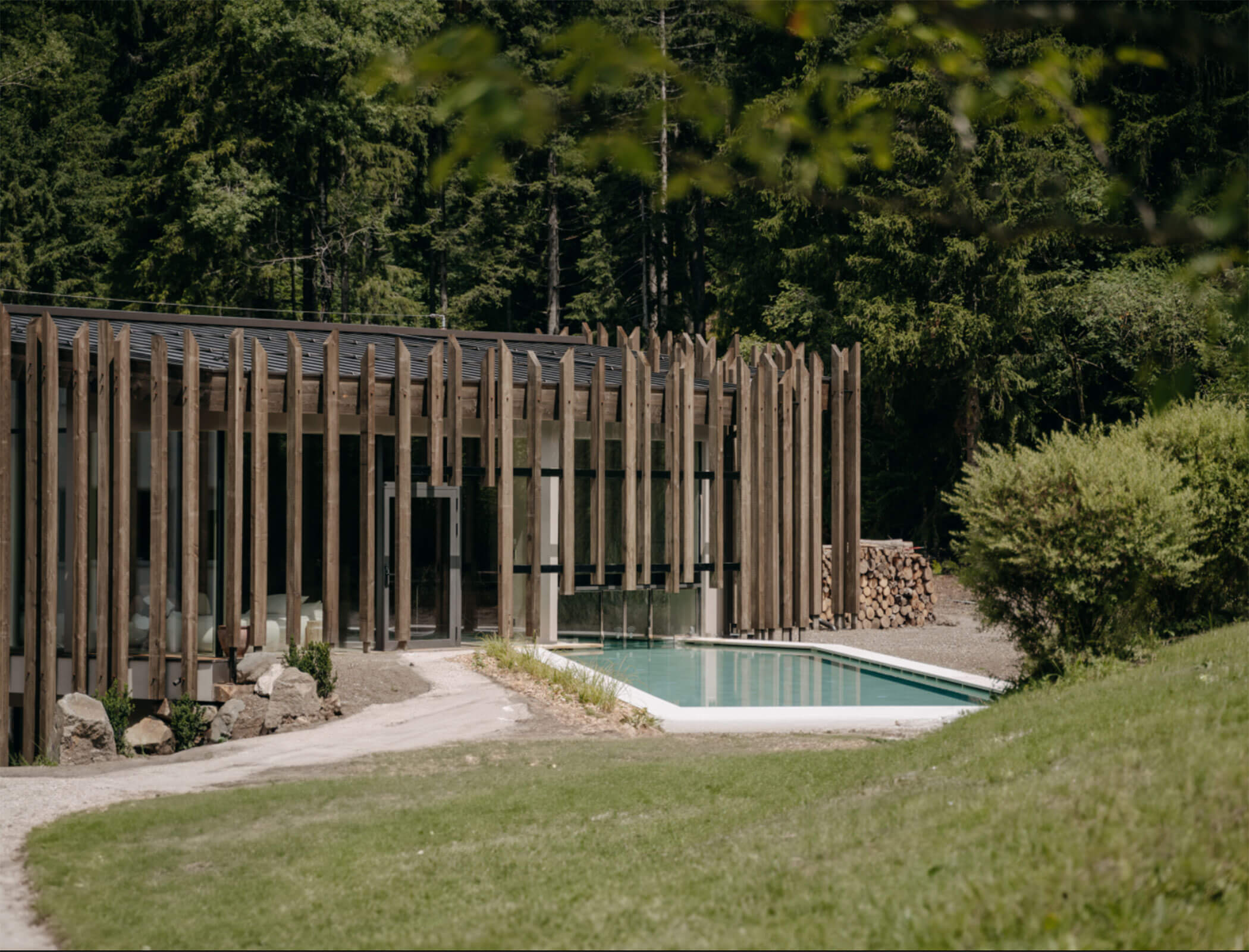 Un prato, la piscina esterna e la facciata in legno della piscina interna - Bad Ratzes
