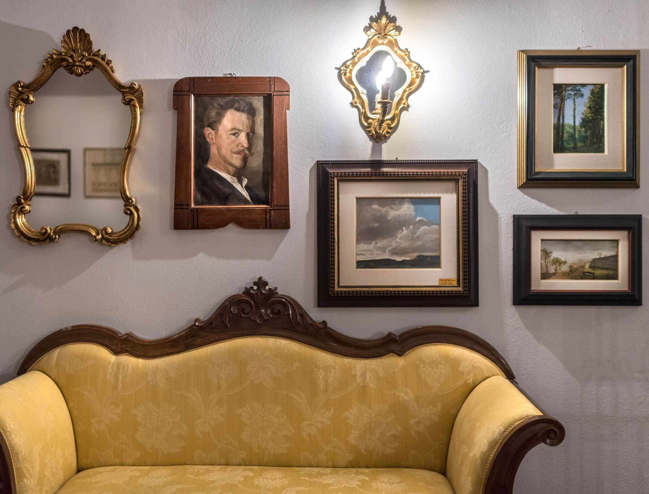 Diversi quadri e uno specchio alla parete, un divano giallo sotto - Bad Ratzes
