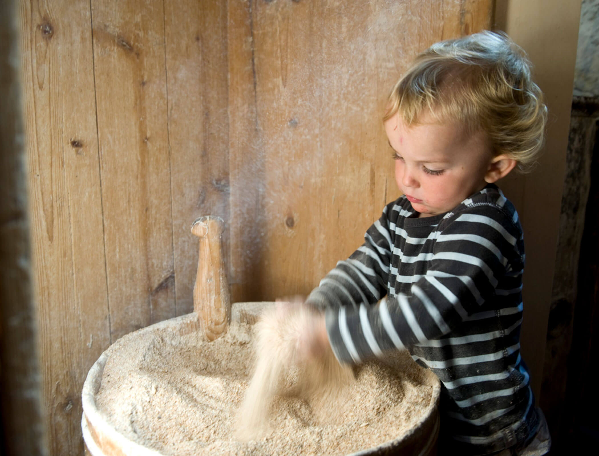 Un bambino affonda le mani in una ciotola di legno piena di sabbia - Bad Ratzes